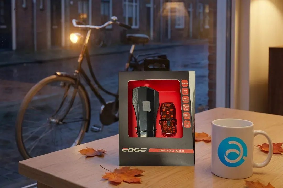 Een fietsverlichtingsset van EDGE op een tafel bij het raam, met buiten een fiets met brandende lamp